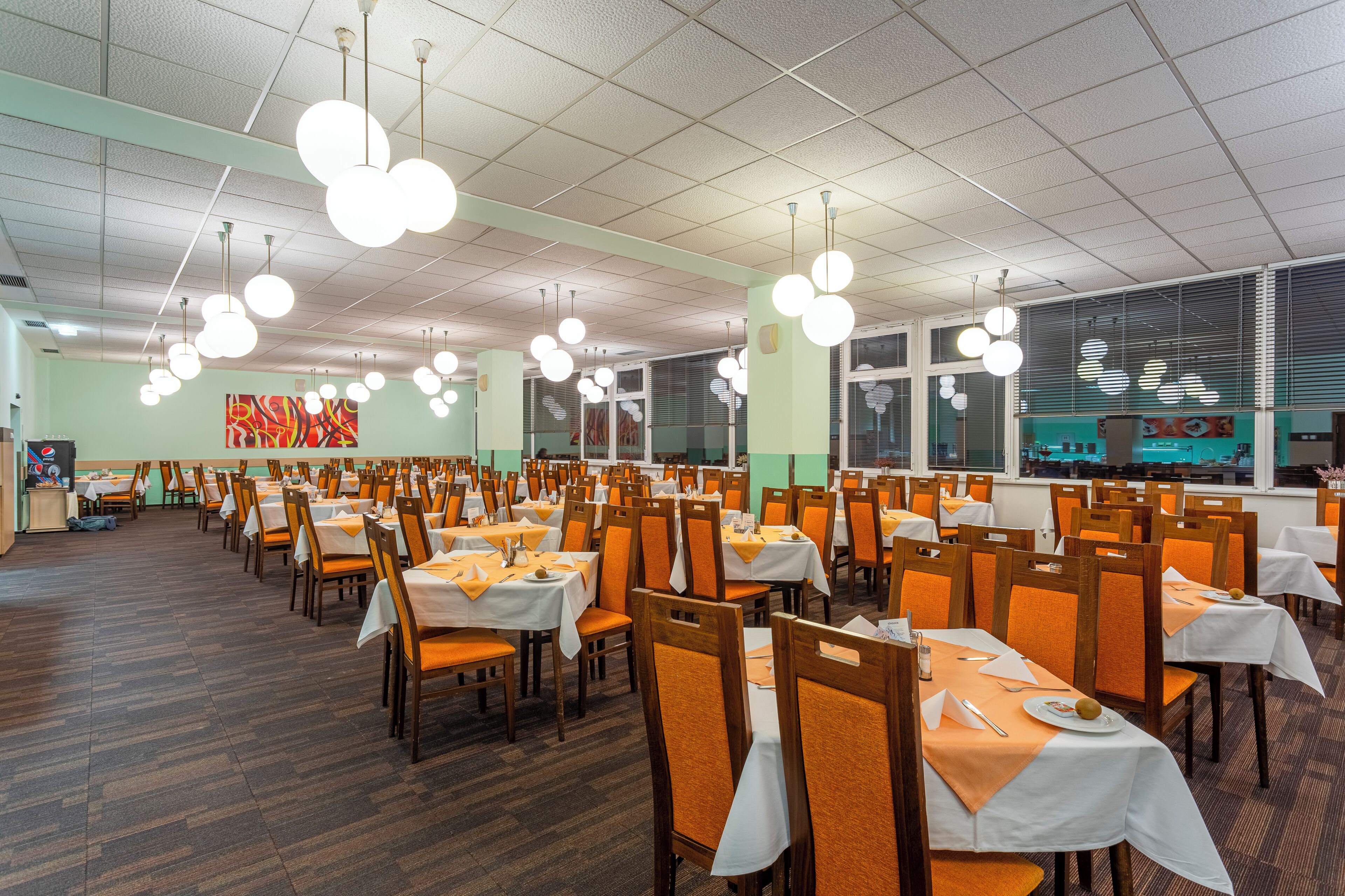A dining area with multiple tables and chairs, white tablecloths, and hanging spherical light fixtures.