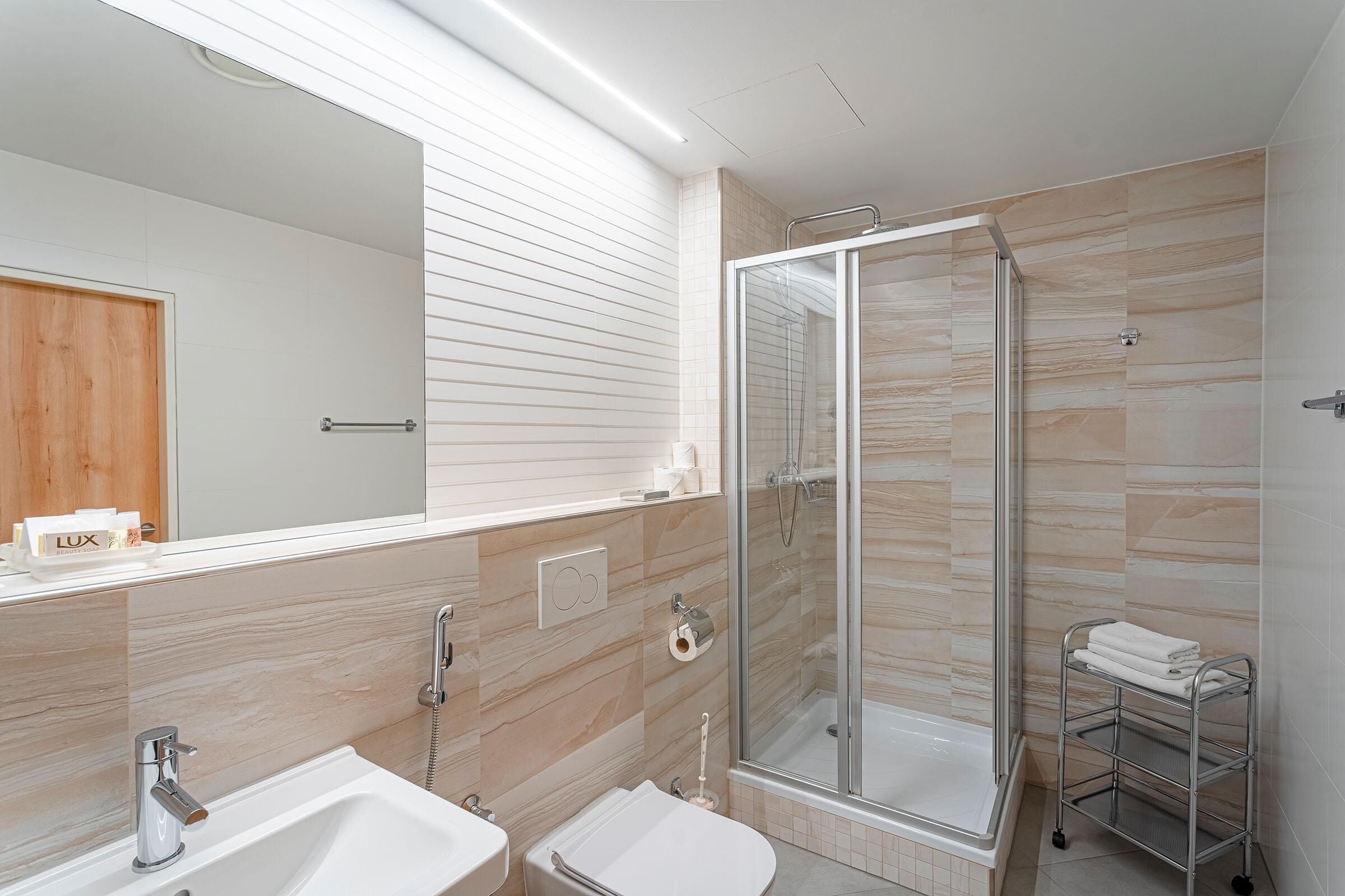 A modern bathroom with a glass-enclosed shower, a large mirror, and a vanity with a sink and towel rack.
