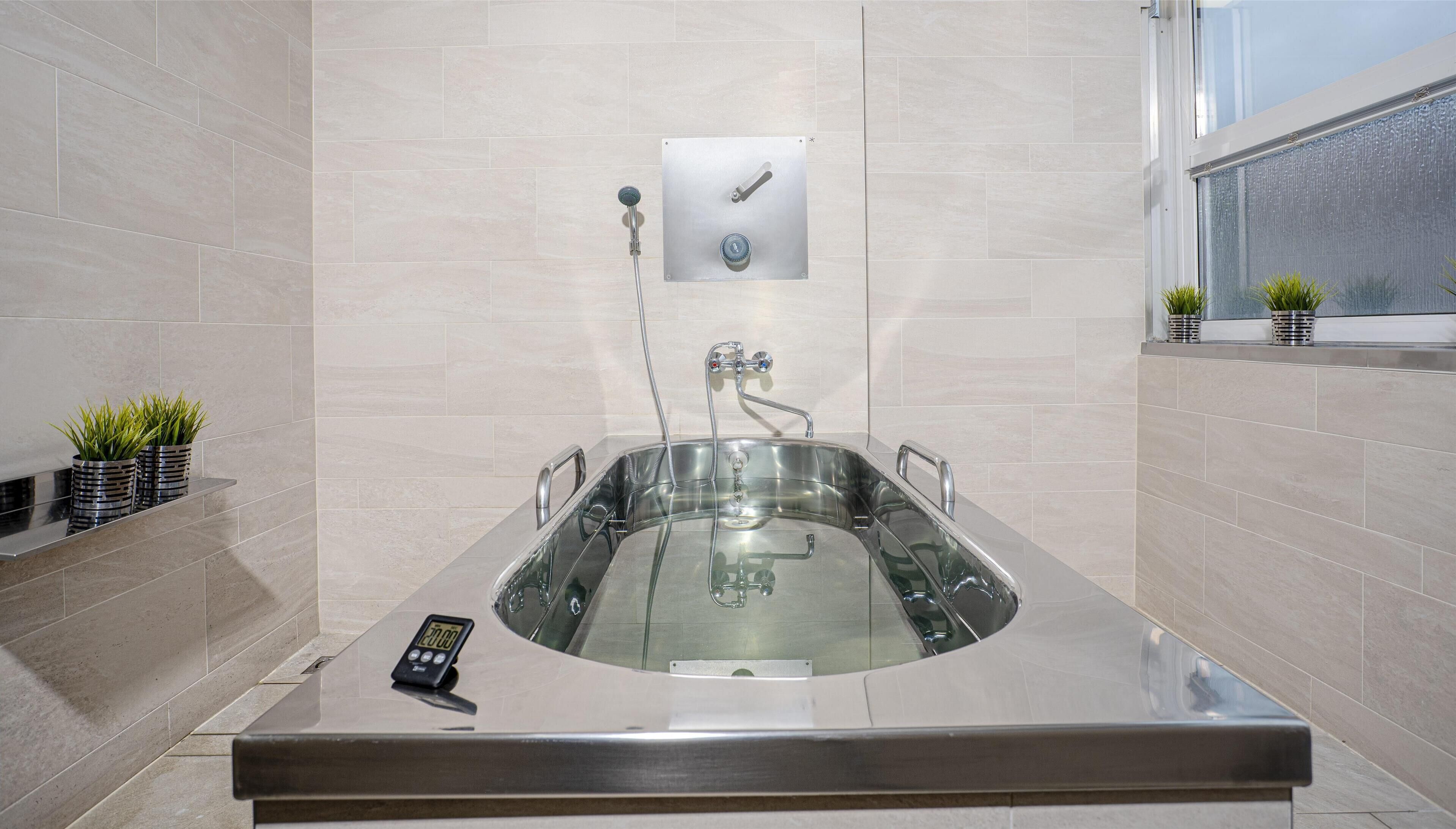 A modern bathroom with a large, rectangular bathtub, a digital shower timer, and a window with a view.