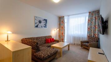 Una sala de estar con un sofá, dos mesitas auxiliares, una mesa de centro, un sillón y un televisor montado en la pared.