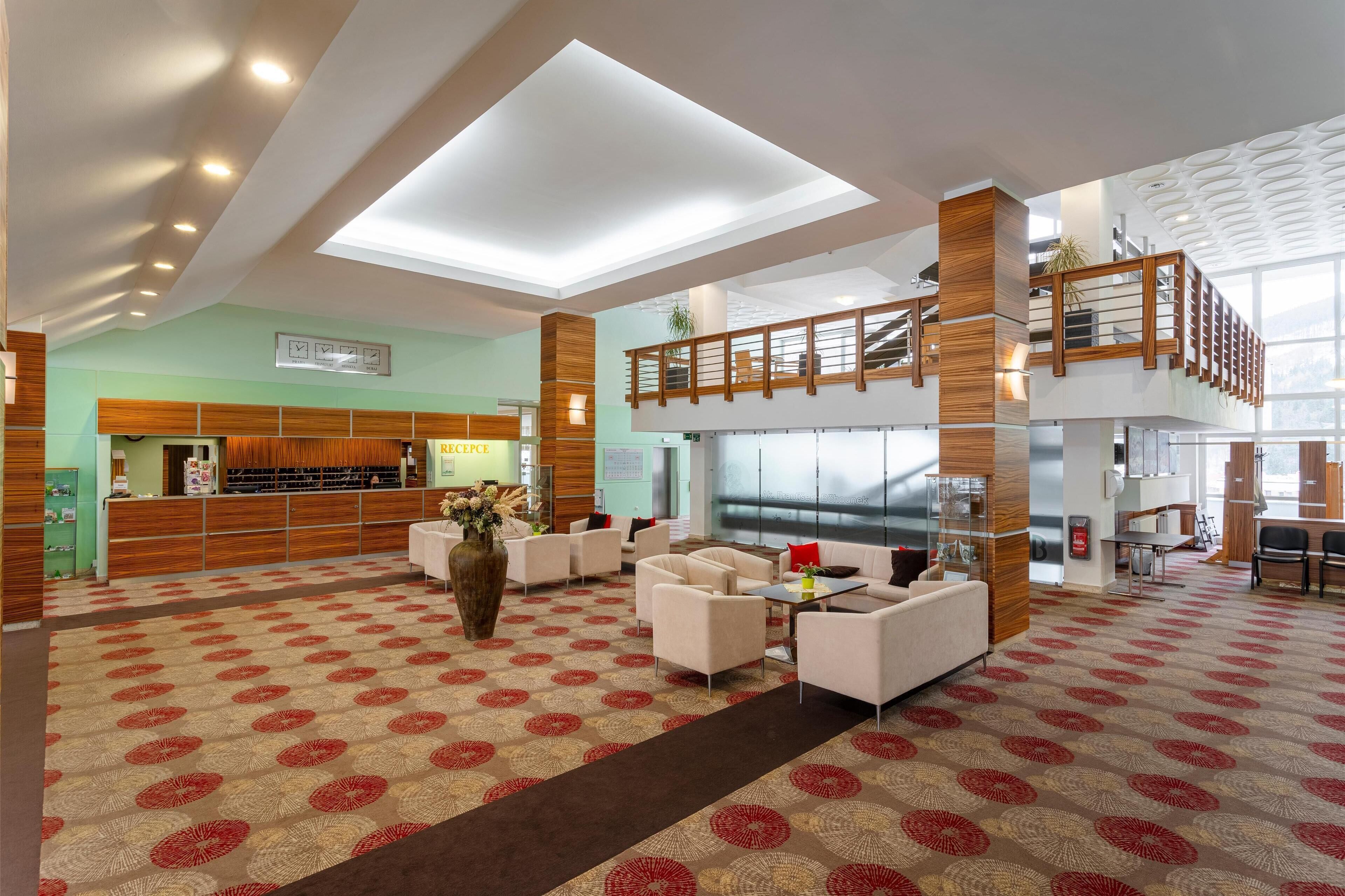 A spacious lobby with a reception desk, seating area, and a staircase to an upper level.