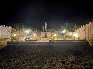 Un espacio al aire libre de noche con una estatua, bancos de madera y una valla de madera.