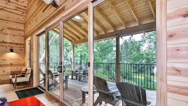 Eine Holzhütte mit überdachter Veranda, großen Fenstern und Sitzgelegenheit im Freien.