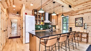Ein Holzblockhaus-Innenraum mit Küche, Barbereich und Esstisch mit Stühlen.