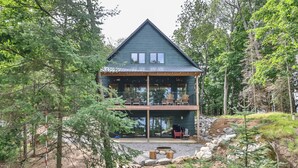 Eine zweistöckige Holzhütte mit Balkon, umgeben von Bäumen und einer natürlichen Landschaft.