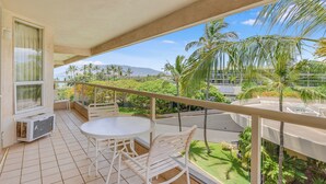 A balcony with a table and chairs, a view of a landscaped garden, and a distant mountain. - Partial Ocean View w/ Lanai, WiFi, Washer/Dryer-G510B (Kihei)