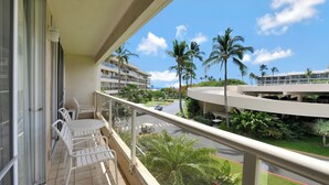 A balcony with white chairs and a table, overlooking a road with palm trees and a multi-story building. - Blissful 1 Bedroom w/lanai, WiFi, and Cable-#H206 (Kihei)