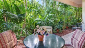 Un porche cubierto con una mesa redonda y sofás a rayas, rodeado de exuberantes plantas tropicales.