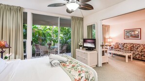 Habitación de hotel con cama, televisión, sofá, zona de comedor con sillas y vistas a zonas verdes.