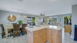 A spacious kitchen with a large island, dining area with wicker chairs, and a view of the outdoors.