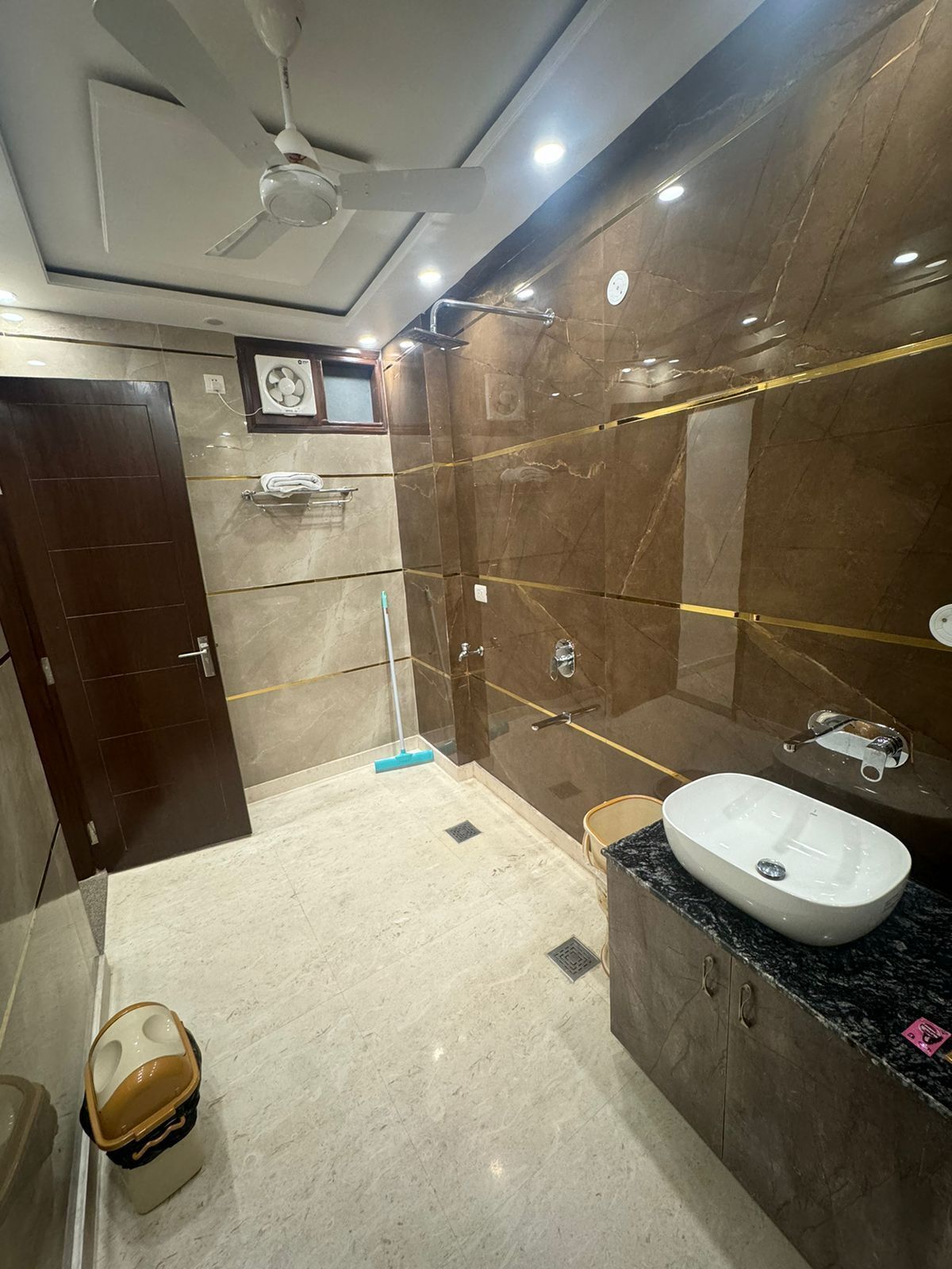 A modern bathroom with a marble floor, a large sink, a shower with glass doors, and a ceiling fan.