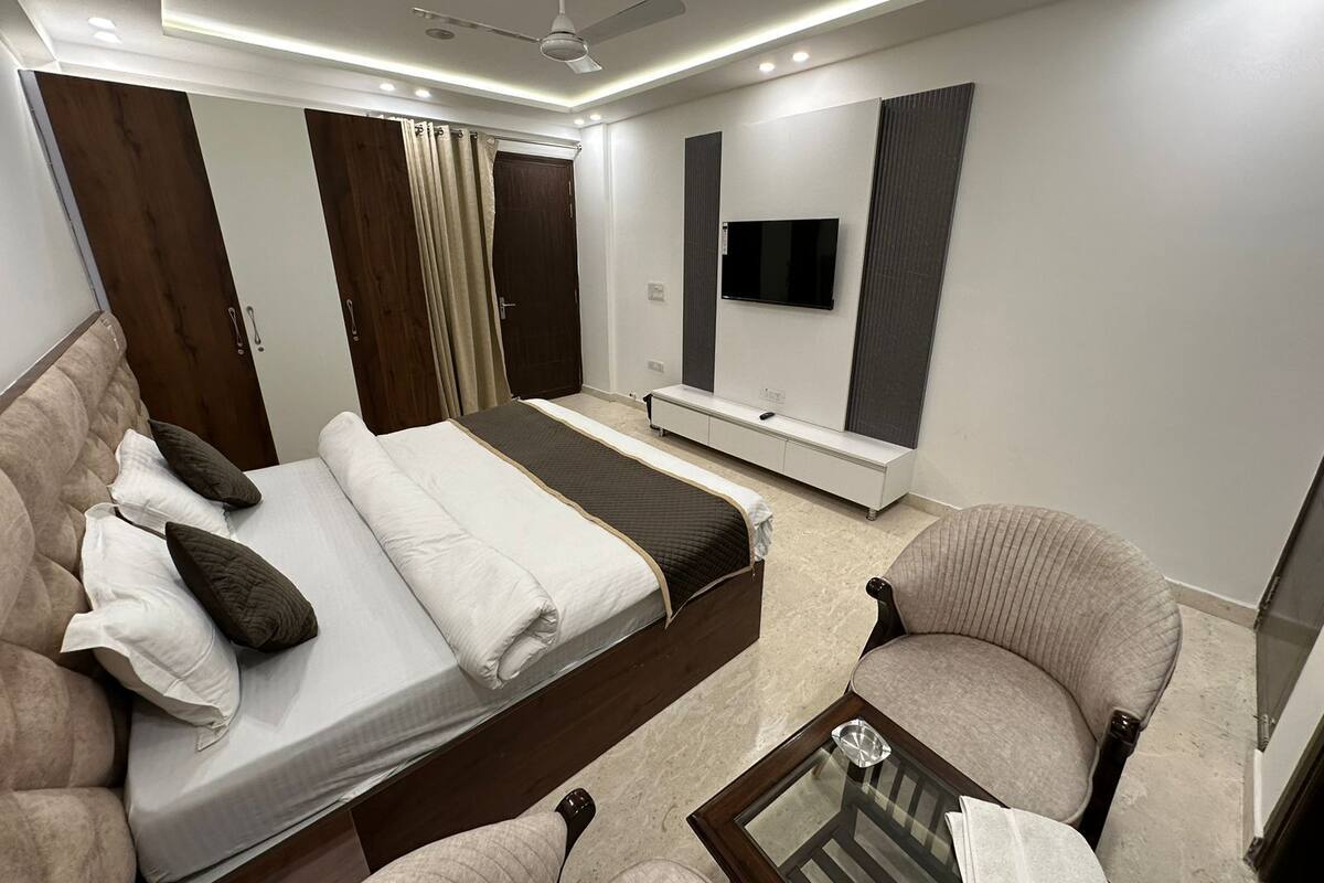 A modern bedroom with a bed, a sofa, a TV, and a ceiling fan.