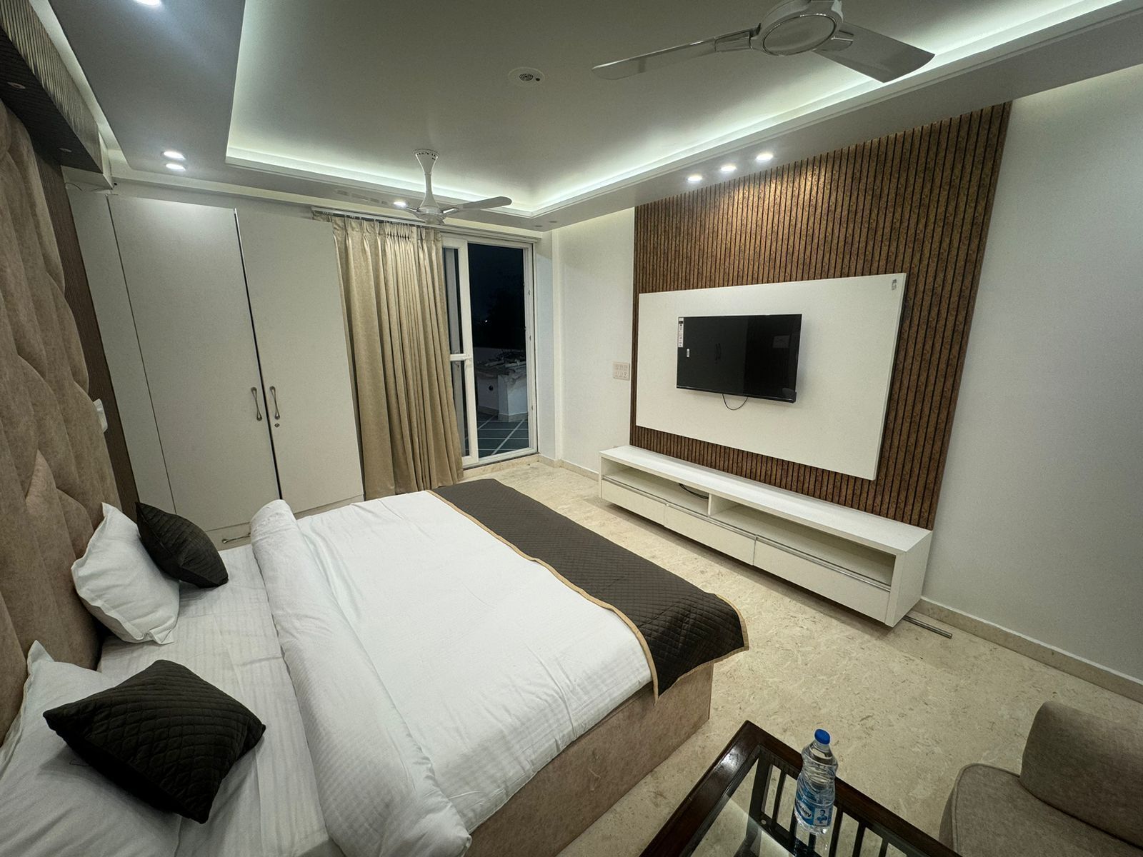 Quarto moderno com cama, televisão, ventoinha no teto e portas de correr.