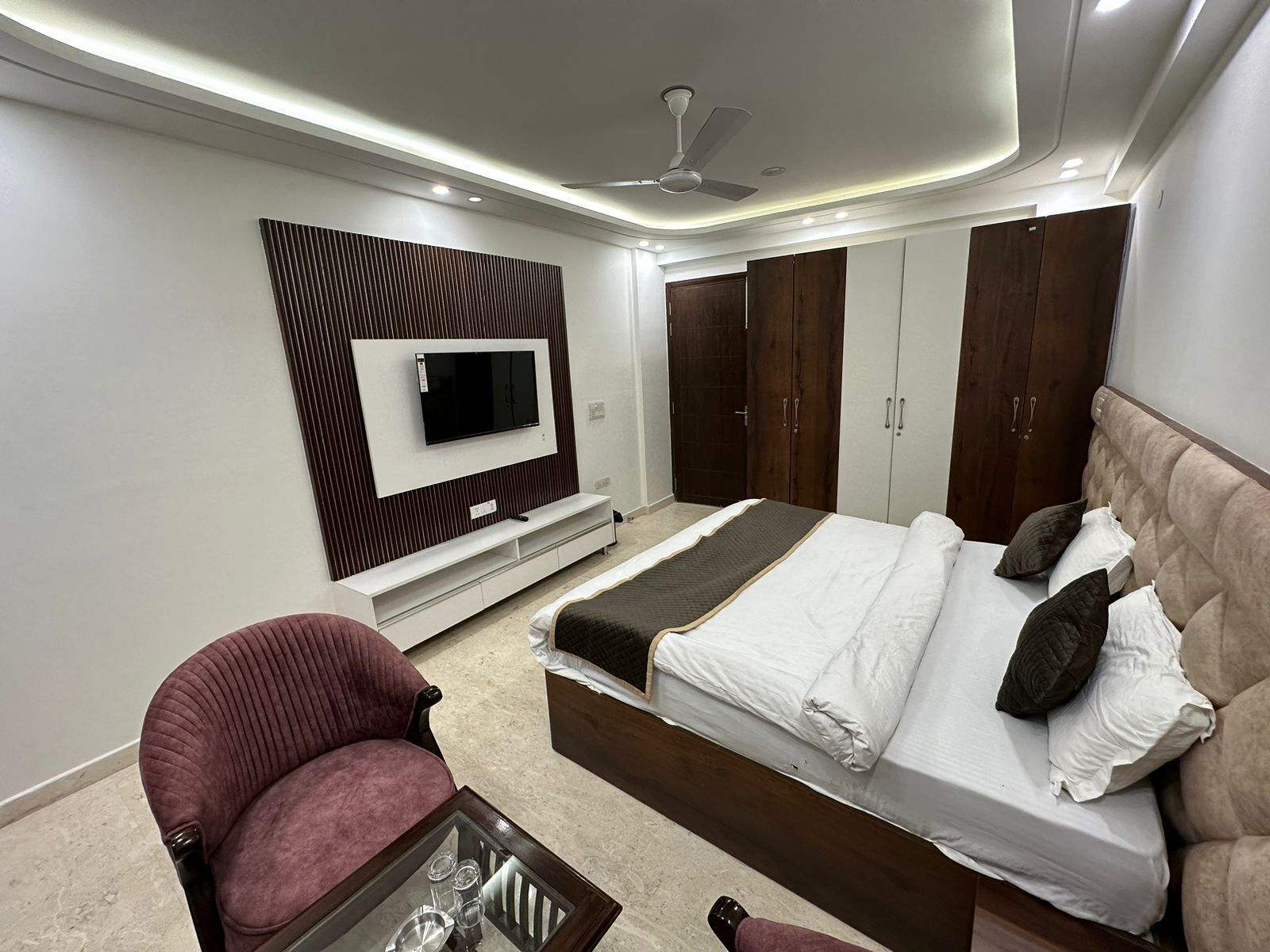 A modern bedroom with a bed, a TV mounted on the wall, a ceiling fan, and built-in wardrobes.