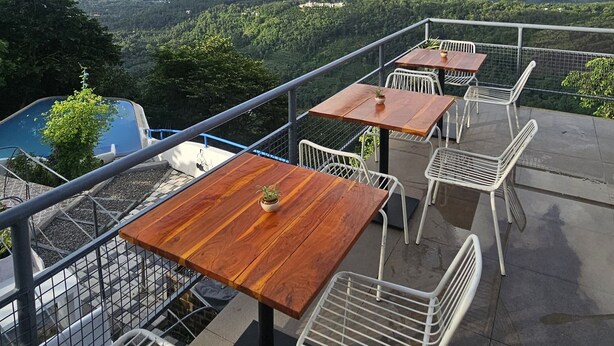 Una terrazza esterna con tavoli in legno e sedie in metallo bianco, con vista su un paesaggio montuoso.