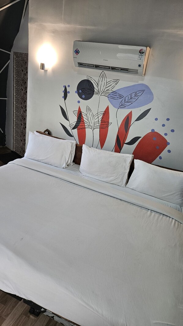 Un lit avec une literie blanche, un climatiseur fixé au mur et un mur décoratif orné de motifs floraux abstraits.