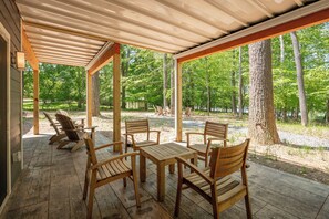 Zona relax all'aperto, riparata, con mobili in legno e vista su un paesaggio boschivo.