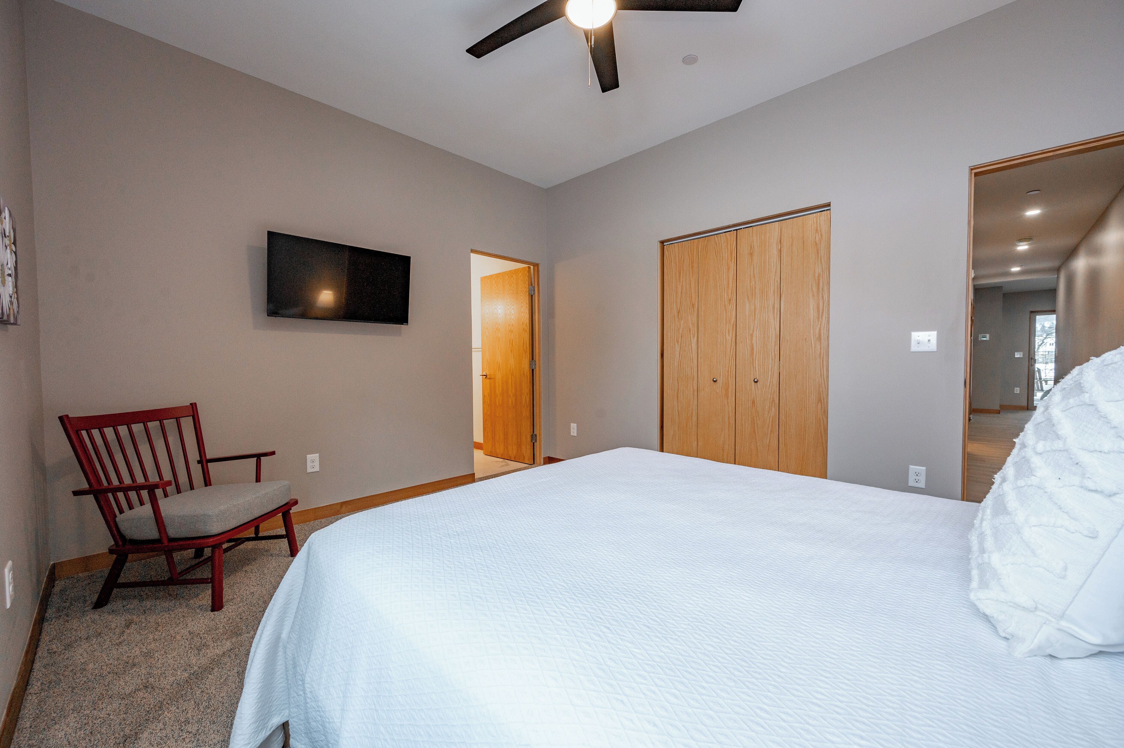 Een slaapkamer met een bed, een stoel, een plafondventilator en een aan de muur bevestigde televisie.