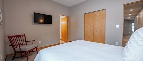 Een slaapkamer met een bed, een stoel, een plafondventilator en een aan de muur bevestigde televisie.