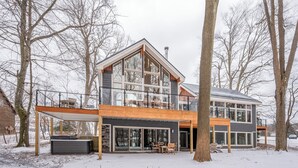 A modern two-story house with large windows, a covered patio, and a hot tub.