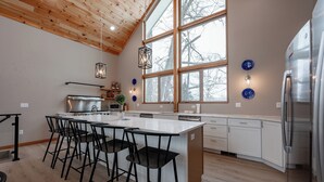 A modern kitchen with a large island, black bar stools, stainless steel appliances, and large windows.