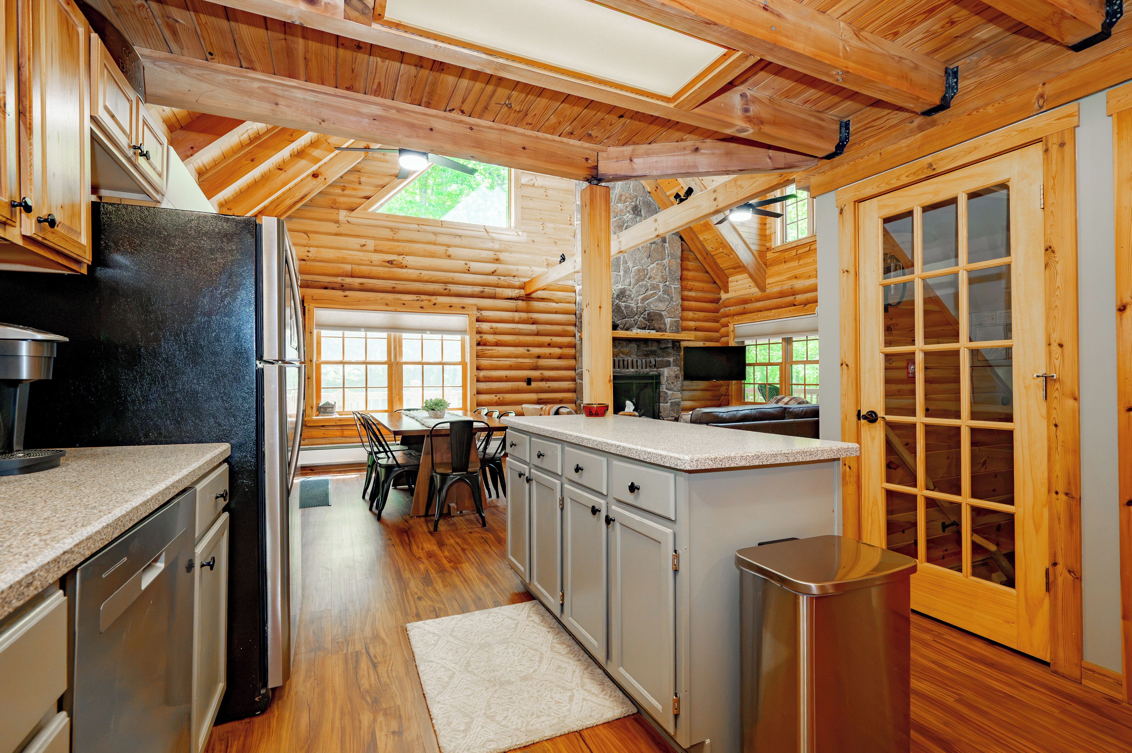 A log cabin interior with a kitchen, dining area, and a stone fireplace.