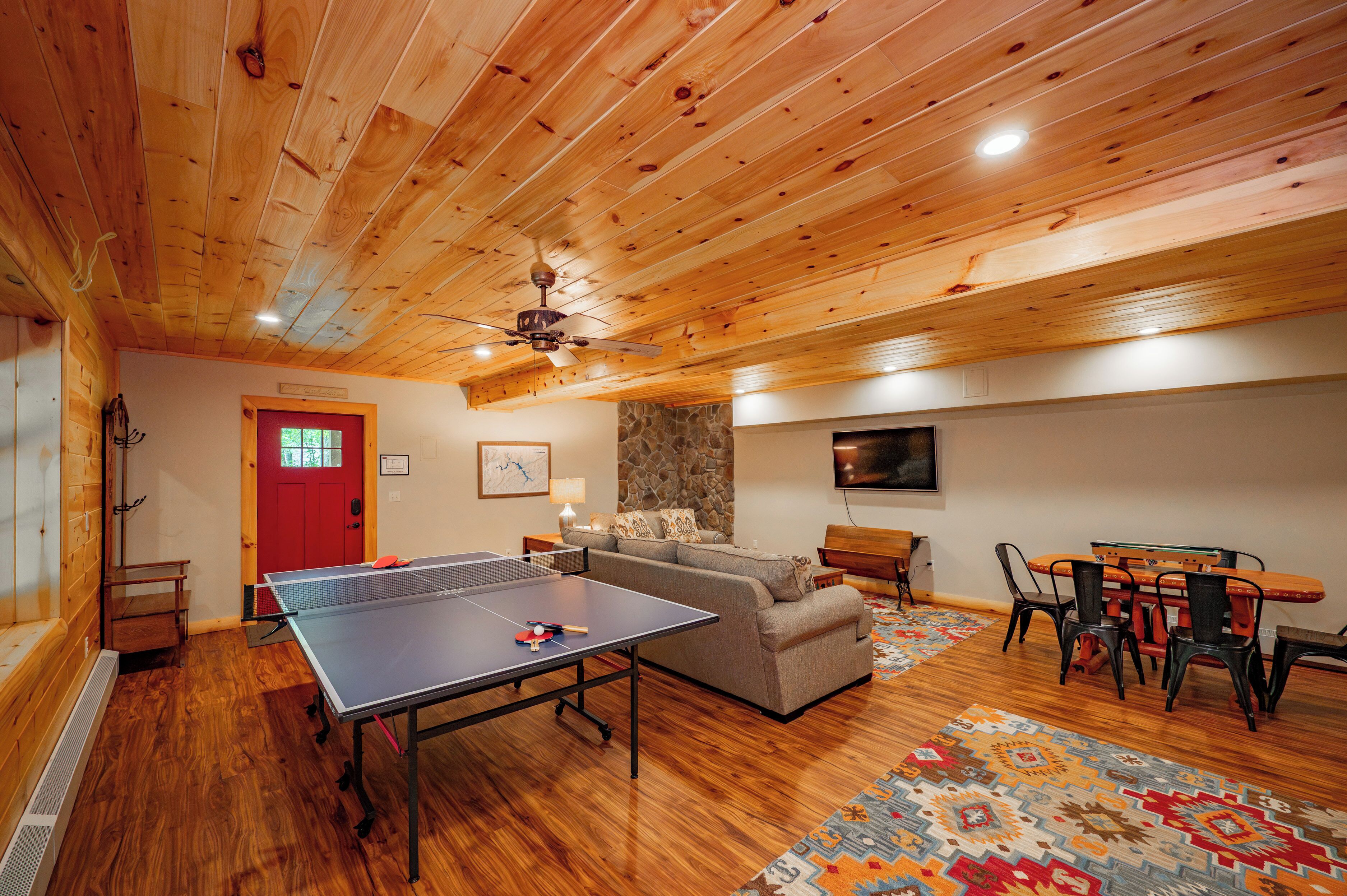 Una habitación con mesa de ping pong, sofá, mesa de comedor con sillas y una pared de piedra decorativa.