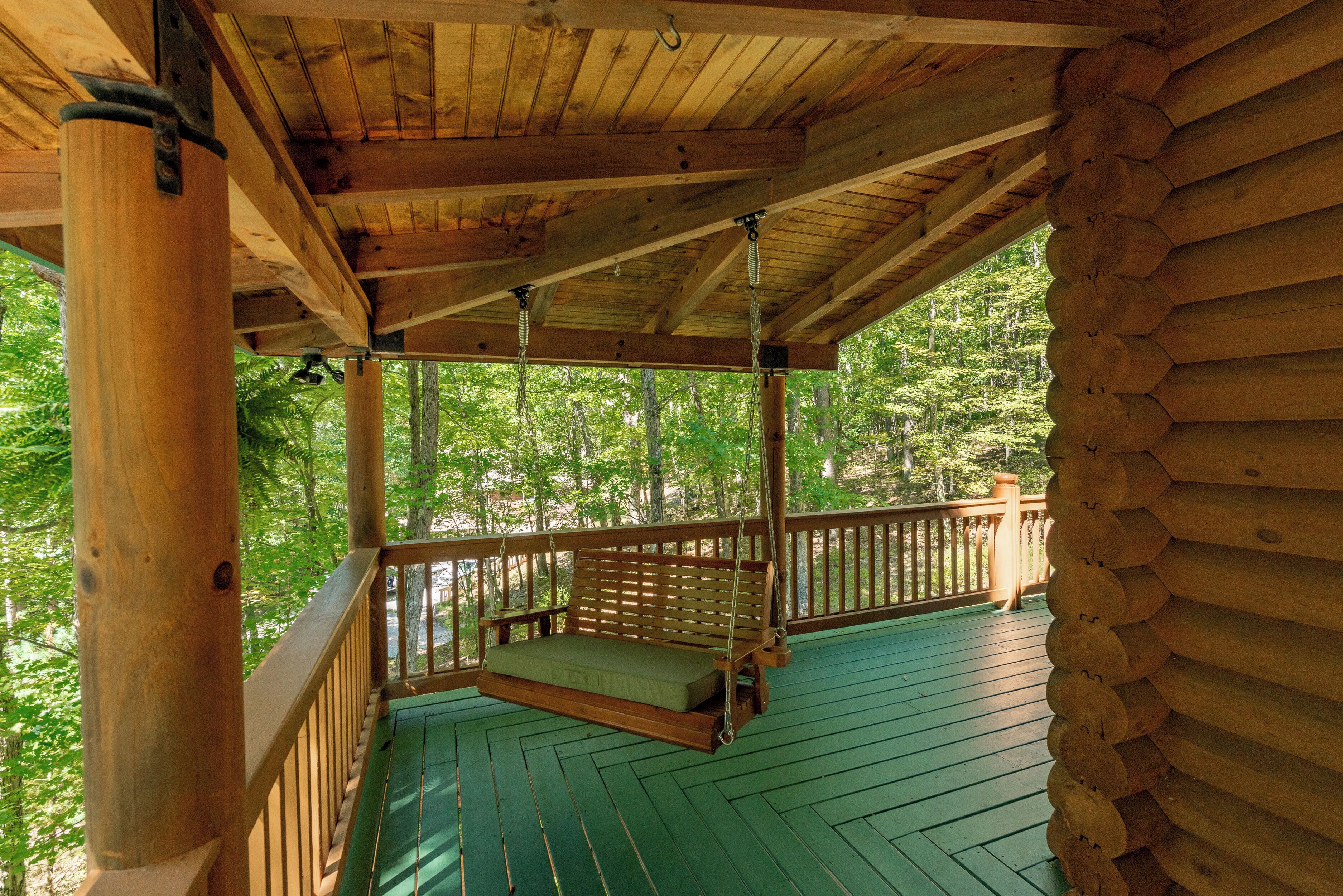A wooden deck with a swing chair and a view of a forest.