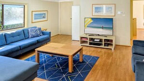 A living room with a blue sofa, a coffee table, and a TV on a stand. - Chill Out at the Basin by Experience Jervis Bay (Basin View)