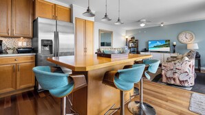 A modern kitchen with wooden cabinets, a stainless steel refrigerator, and a bar area with two stools.