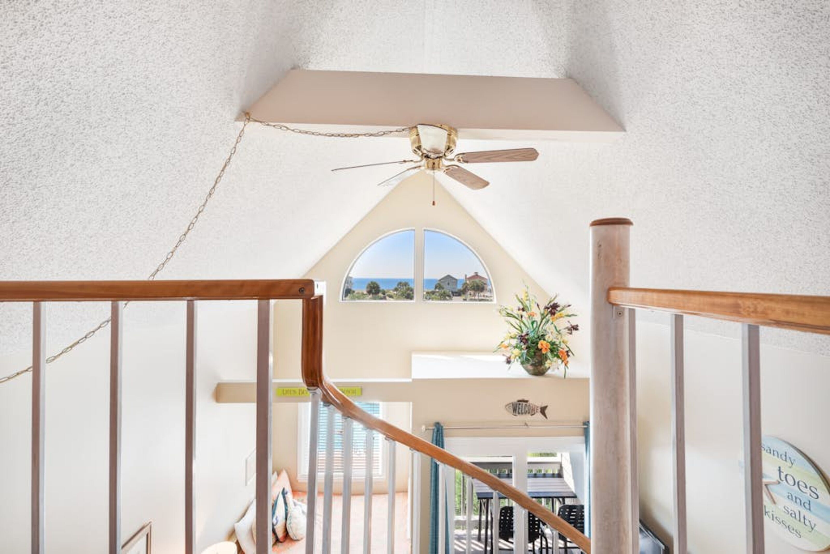 A staircase with a wooden handrail leading to a landing with a ceiling fan and a welcome sign.
