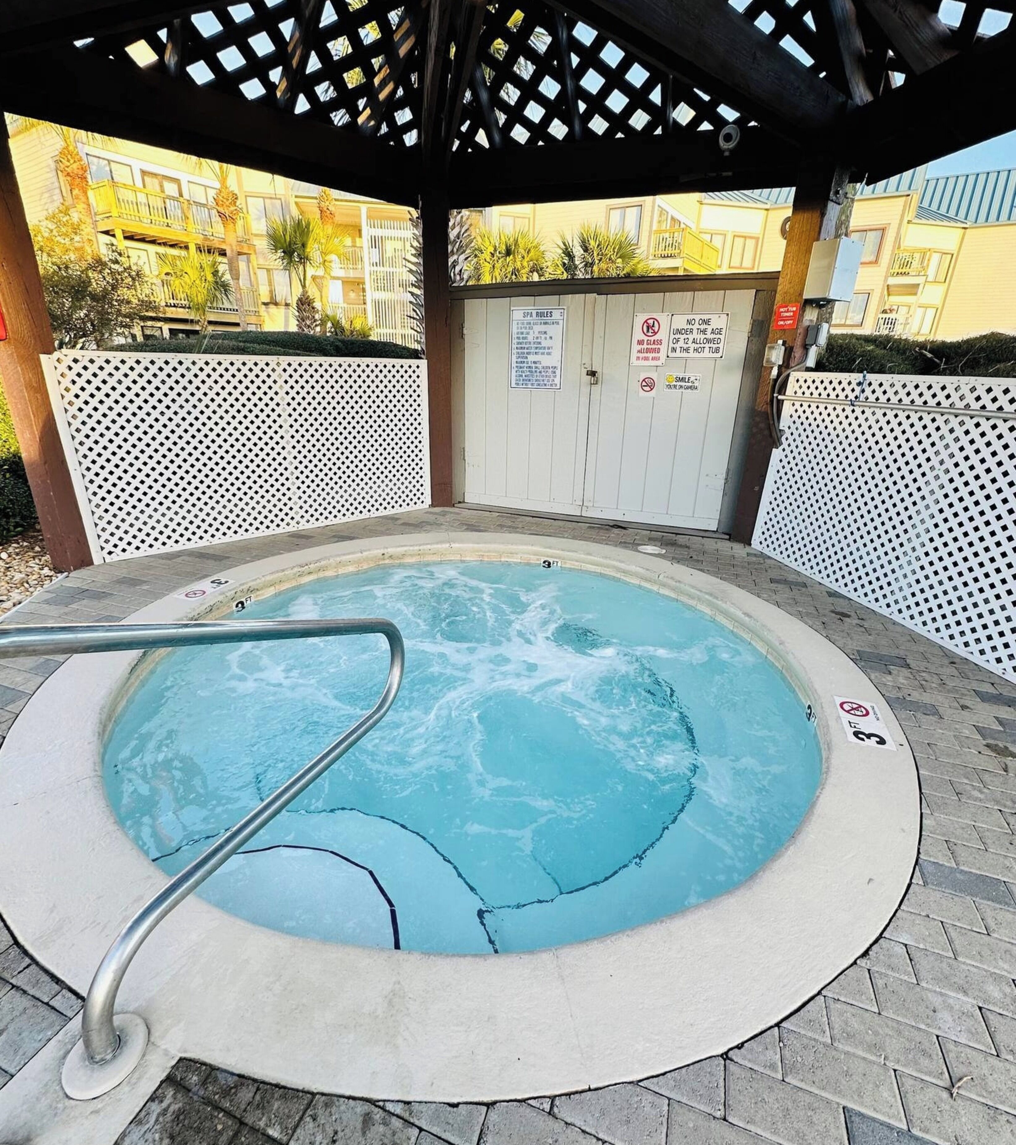 A hot tub under a wooden pergola with a white fence in the background.