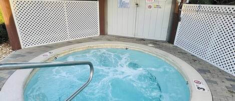 A hot tub under a wooden pergola with a white fence in the background.