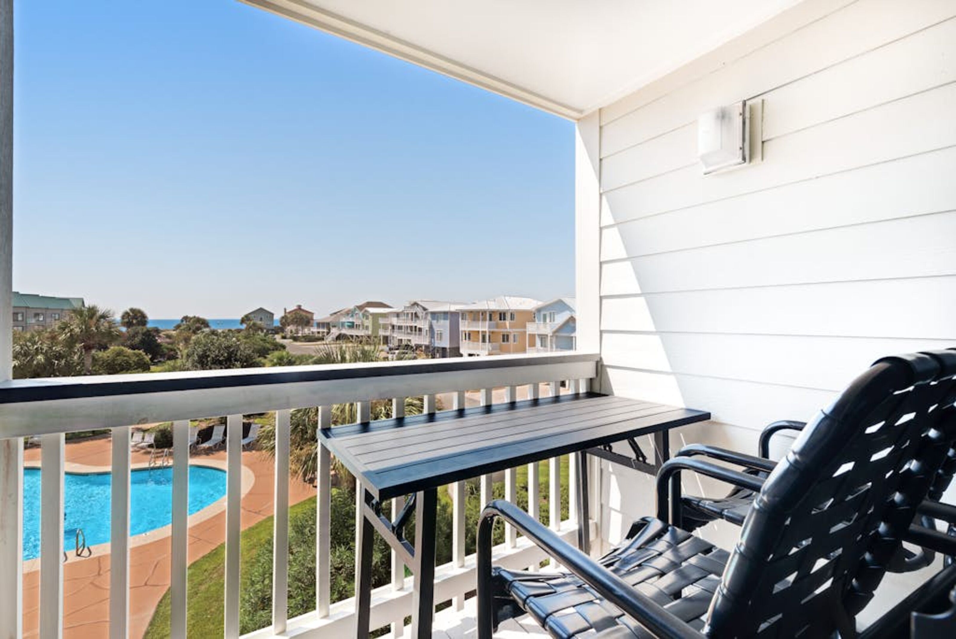 A balcony with a pool view, a table, and two chairs.