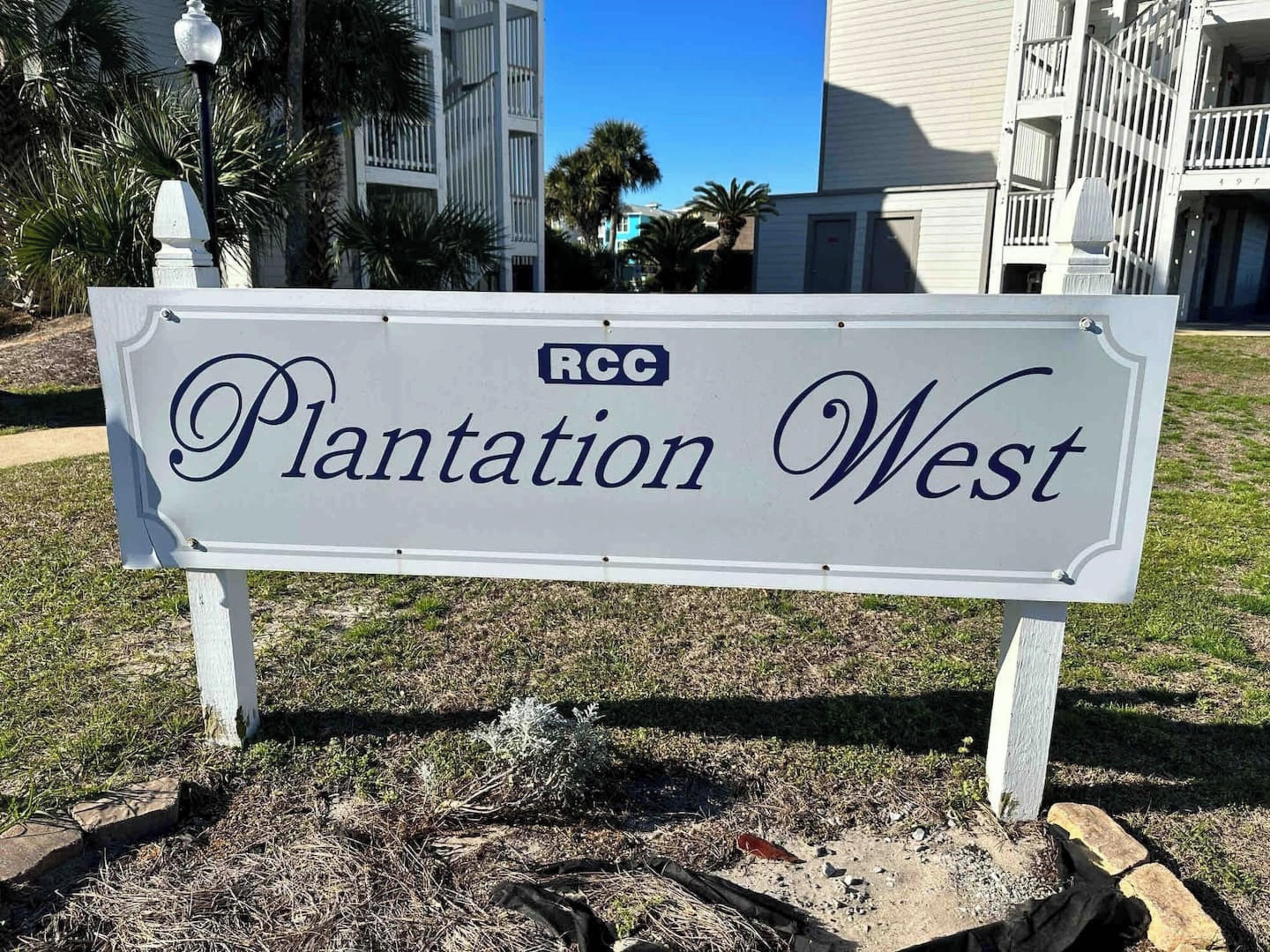 Schild für 'Plantation West' mit freiem Blick auf die umliegenden Gebäude und die angelegte Landschaft.