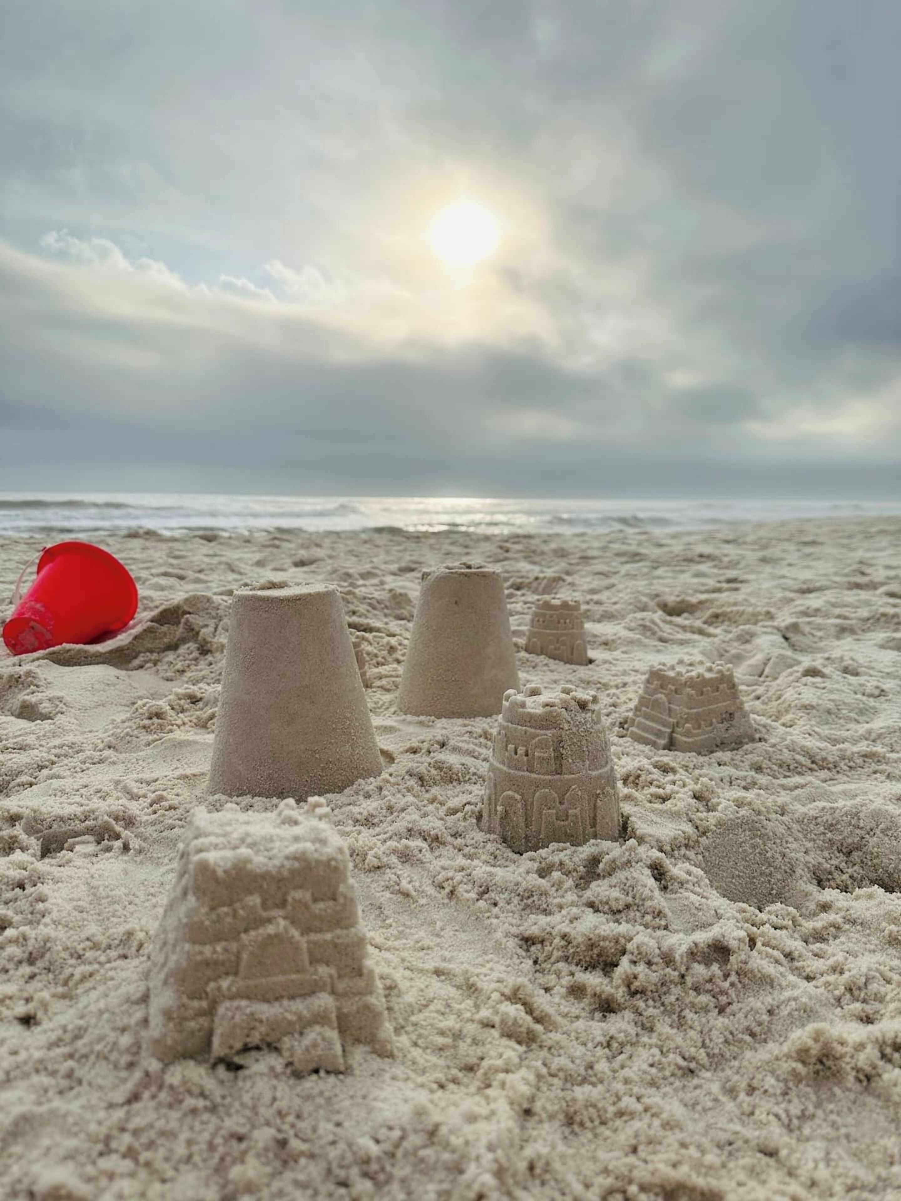 Une plage avec des châteaux de sable et un seau rouge.