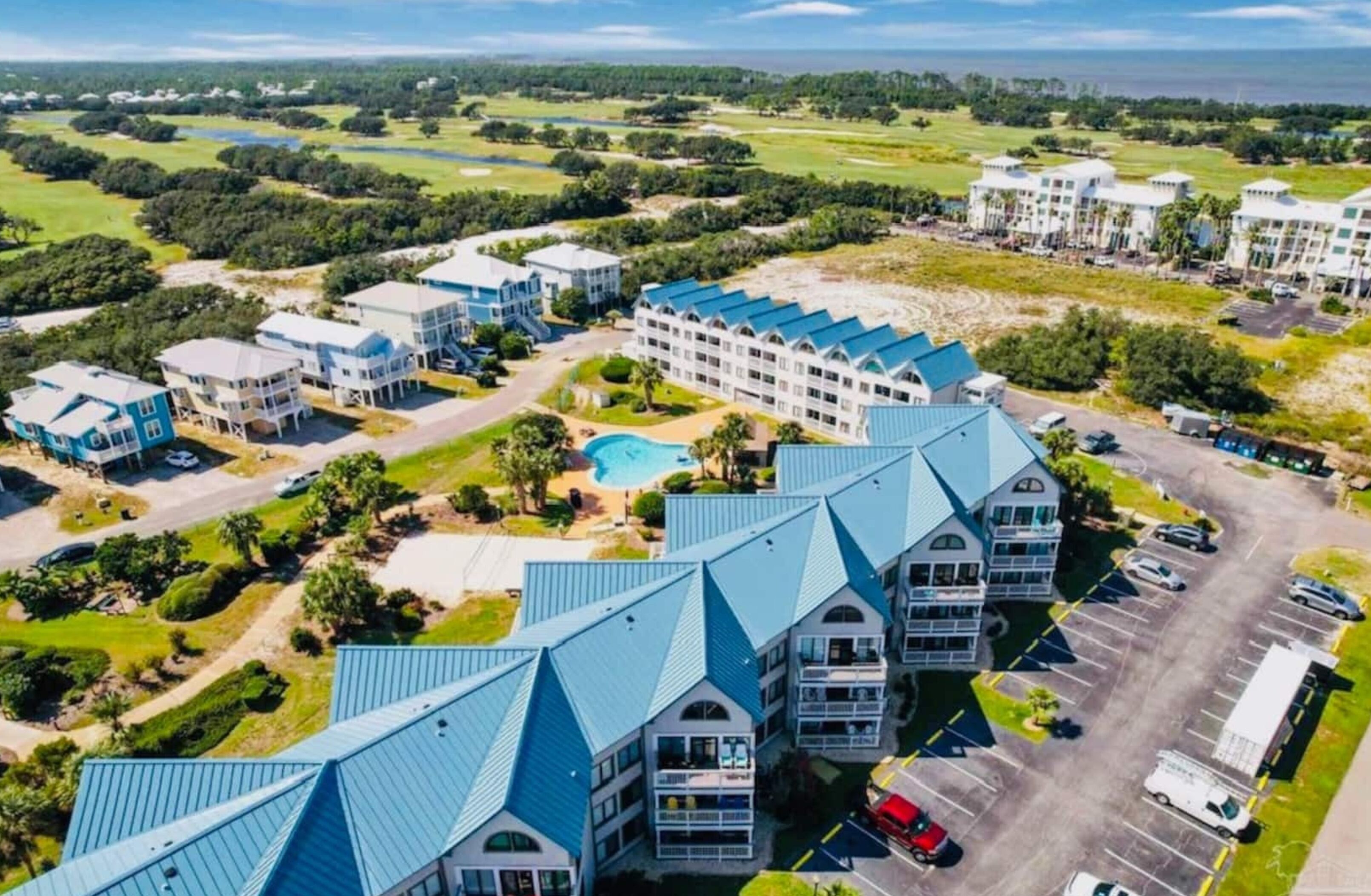 Un resort con varias construcciones, una piscina y un campo de golf al fondo.
