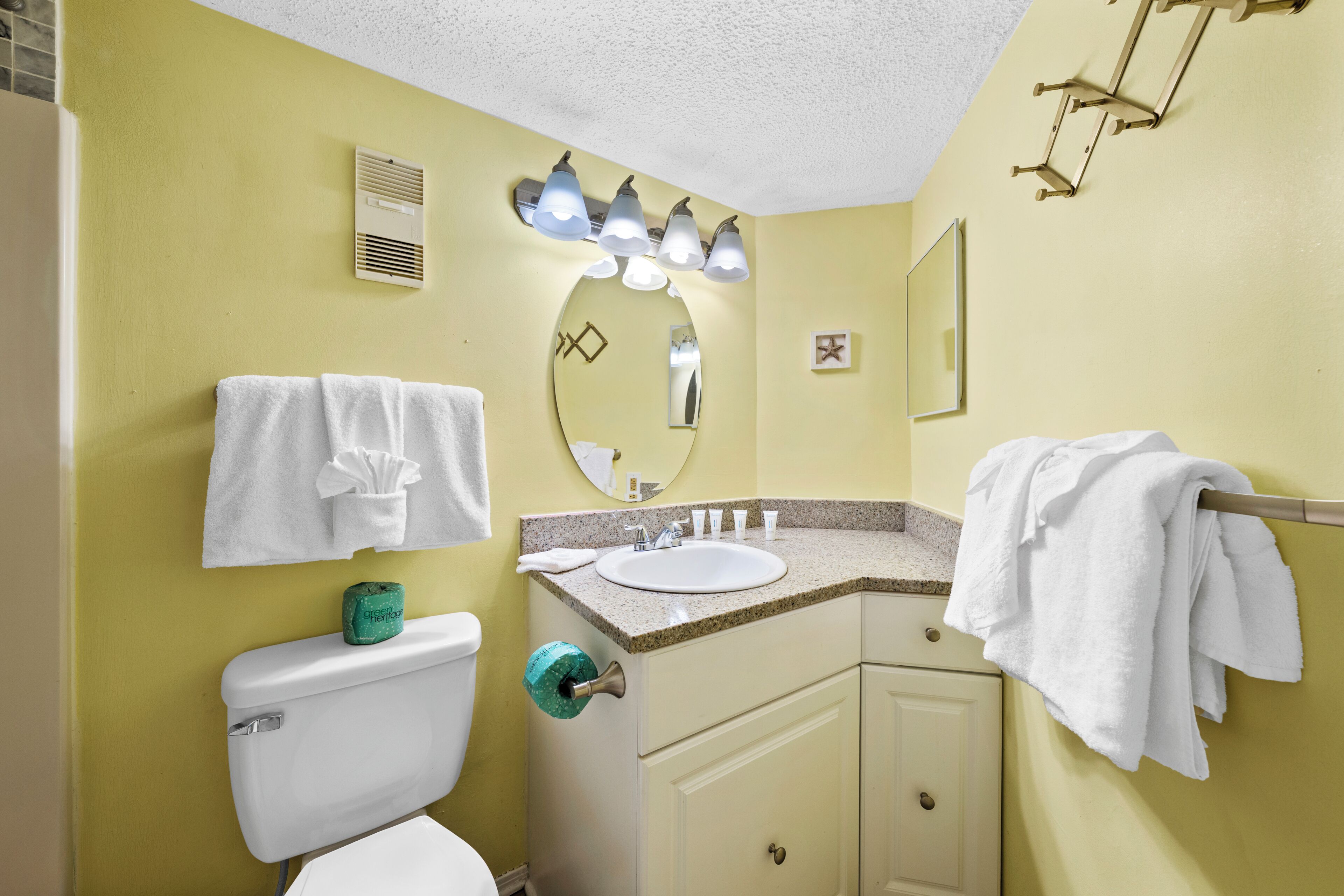 A bathroom with a toilet, sink, mirror, towel rack, and a towel dispenser.