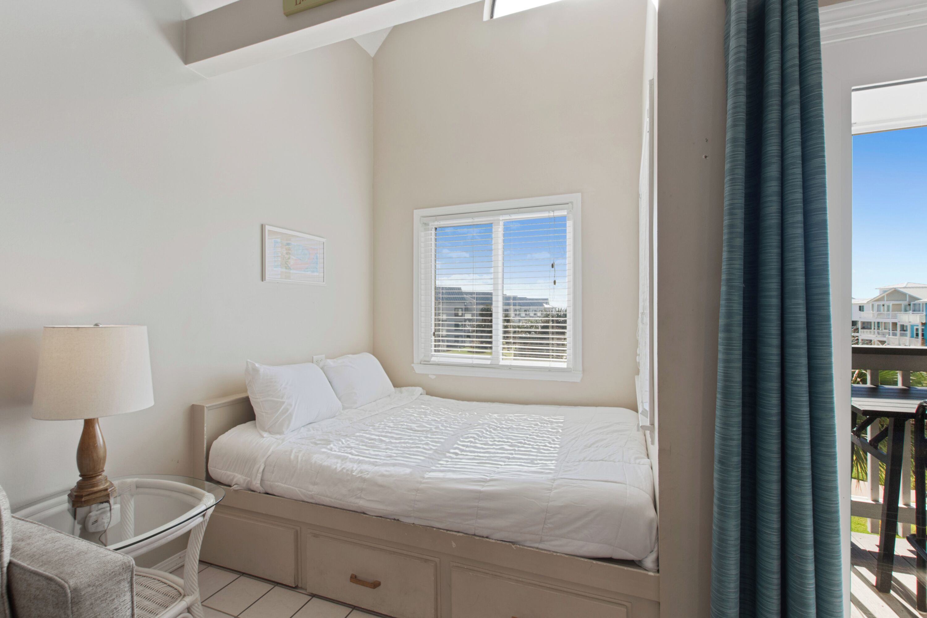 Un dormitorio con cama, mesita de noche con lámpara, una silla y ventana con persianas.