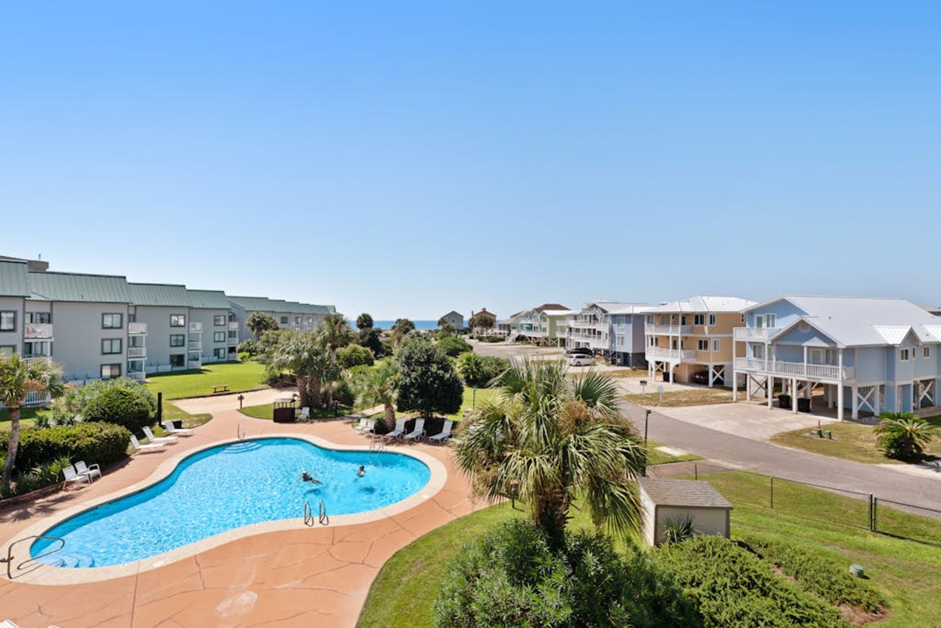 A pool area with a curved design, surrounded by greenery and adjacent to a multi-story building with balconies.