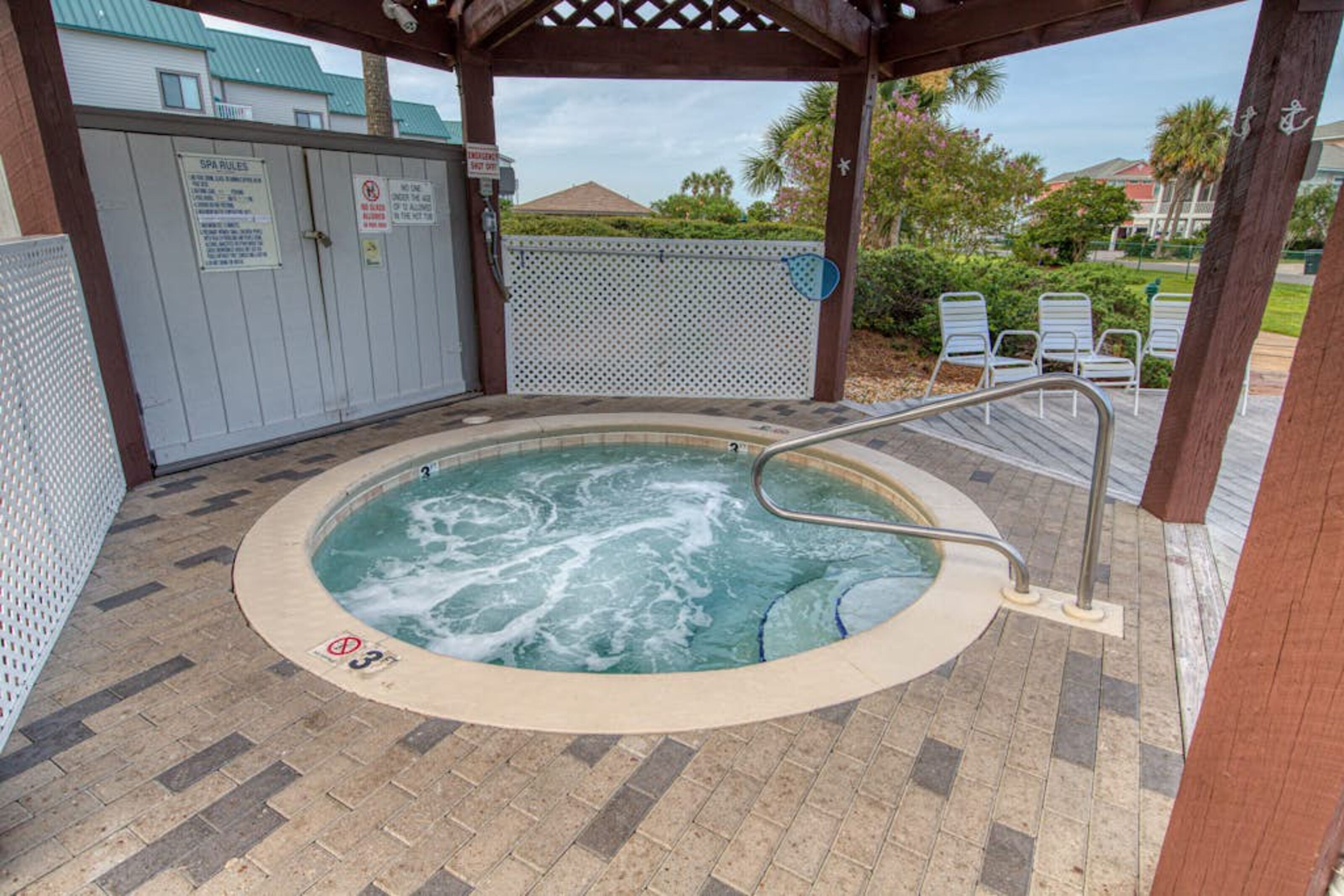 A hot tub area with a wooden pergola, a poolside chair, and a sign indicating spa rules.