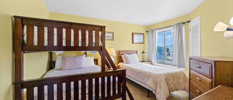 A bedroom with two beds, a wooden headboard, a nightstand, a dresser, and a window with curtains.