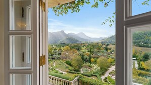 Blick aus einem Zimmer mit großem Fenster auf einen angelegten Garten mit Bergen im Hintergrund.