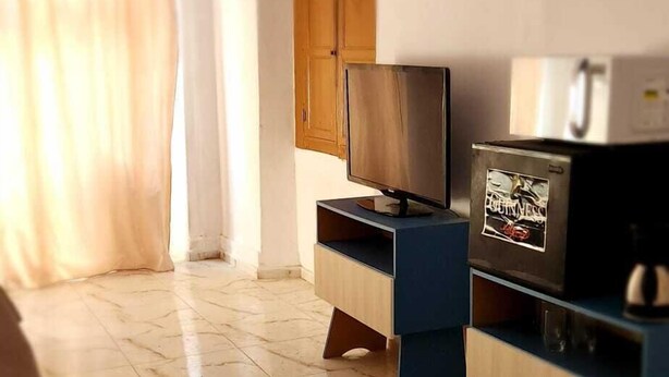 A room with a television on a wooden stand, a refrigerator with a Guinness logo, and a wooden door. - Hospedagem Rio Lapa  (Rio de Janeiro)