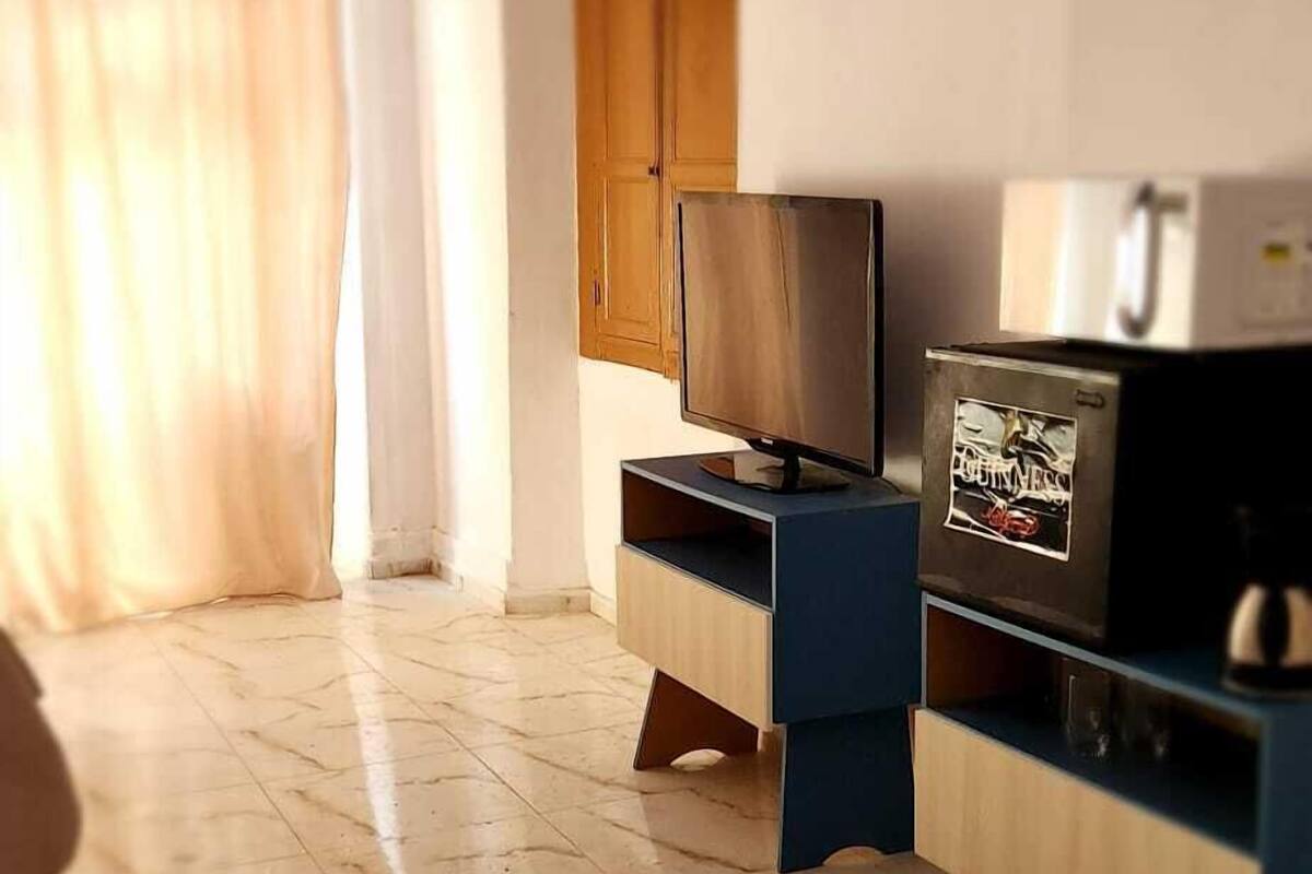 Una habitación con una televisión sobre un soporte de madera, un refrigerador con el logotipo de Guinness y una puerta de madera.