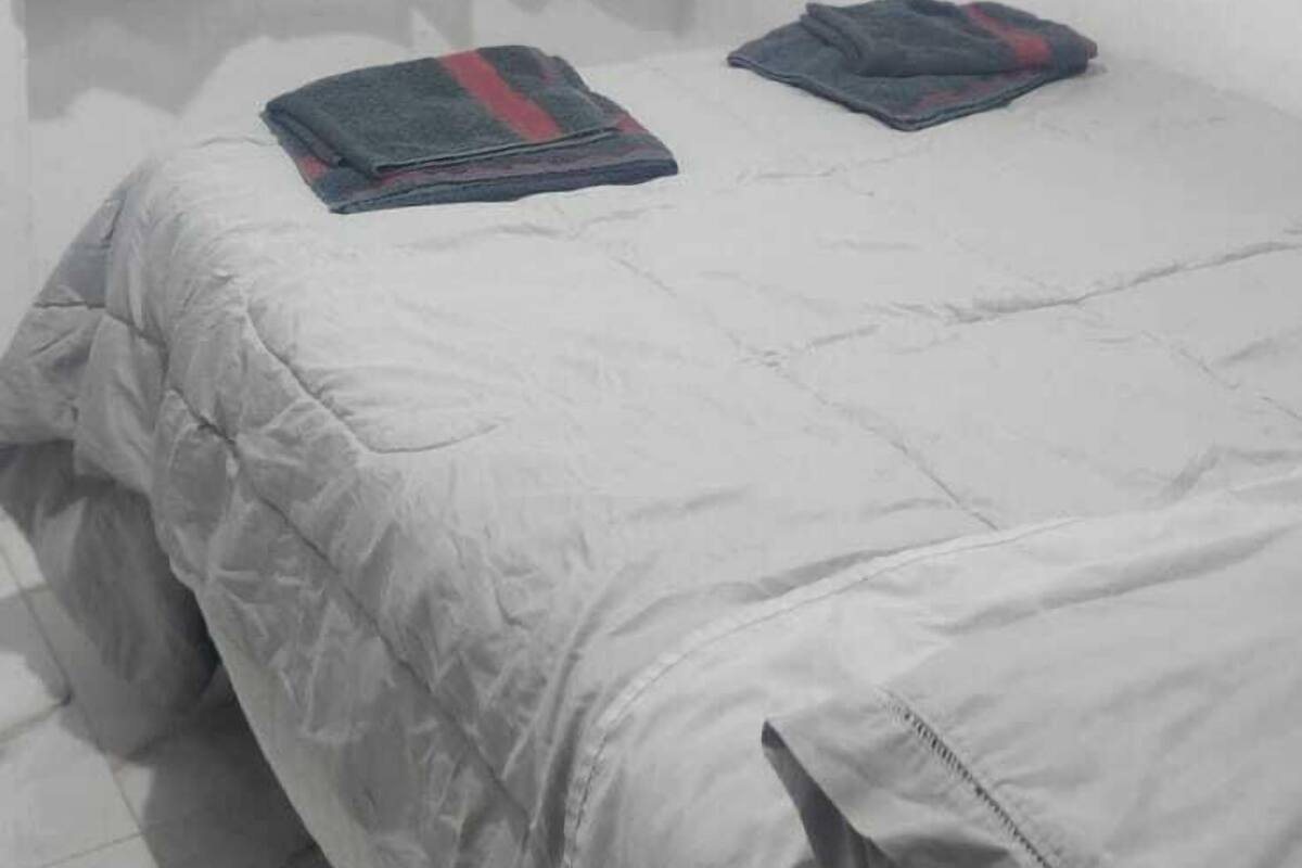 Una cama individual con edredón gris y dos toallas dobladas encima.