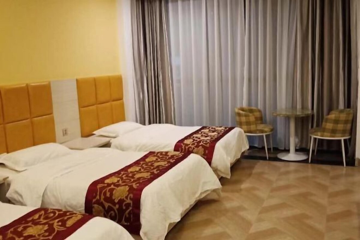 Ein Hotelzimmer mit zwei Betten, einem Kopfteil, einem kleinen runden Tisch, zwei Stühlen und einem fenster mit Vorhängen.
