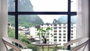 Ein Zimmer mit Blick auf Berge und Gebäude, ausgestattet mit einem runden Tisch, Stühlen und einer Pflanze in einer Vase.