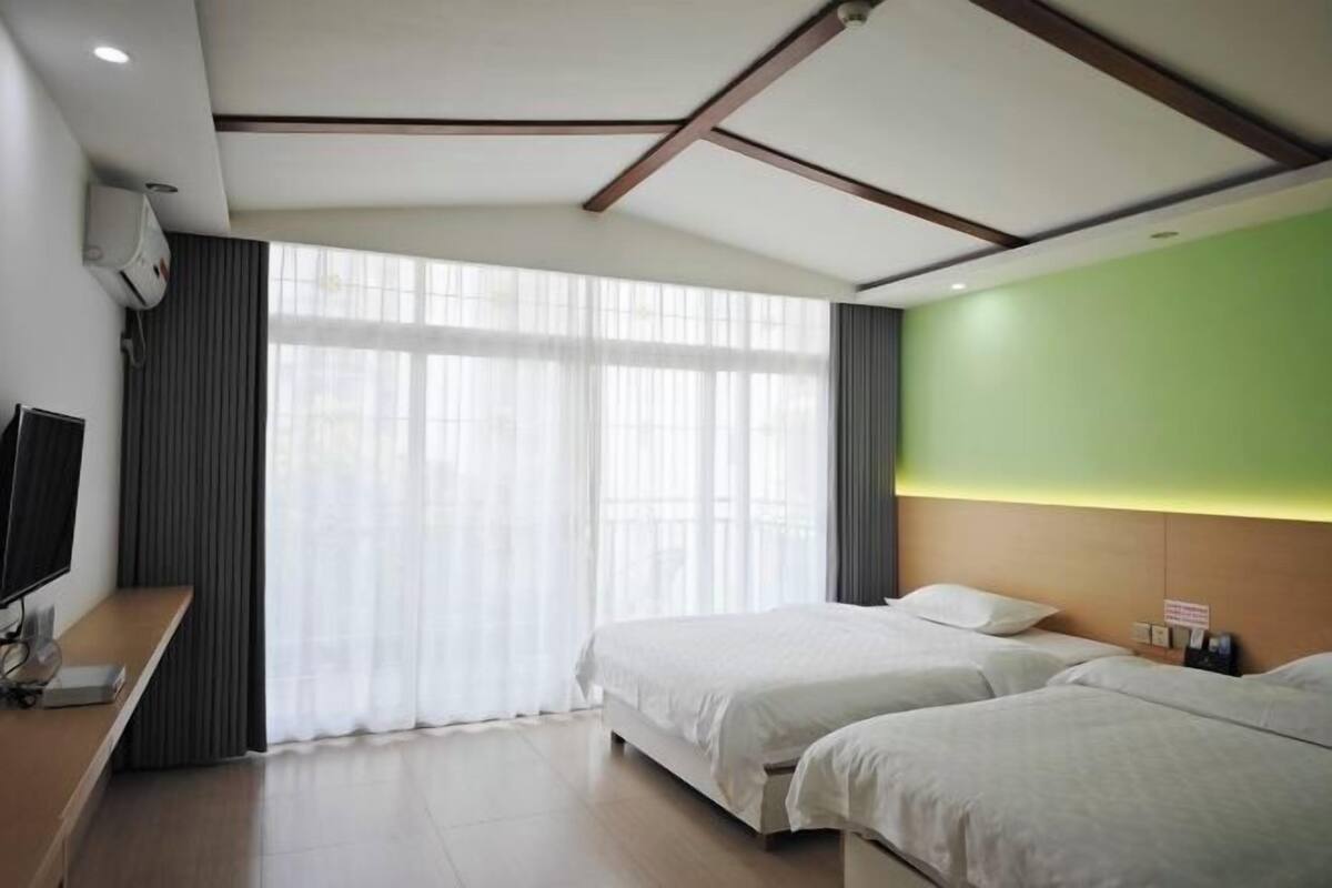 Habitación de hotel con un ventanal grande, un televisor de pantalla plana, un escritorio de madera y dos camas.