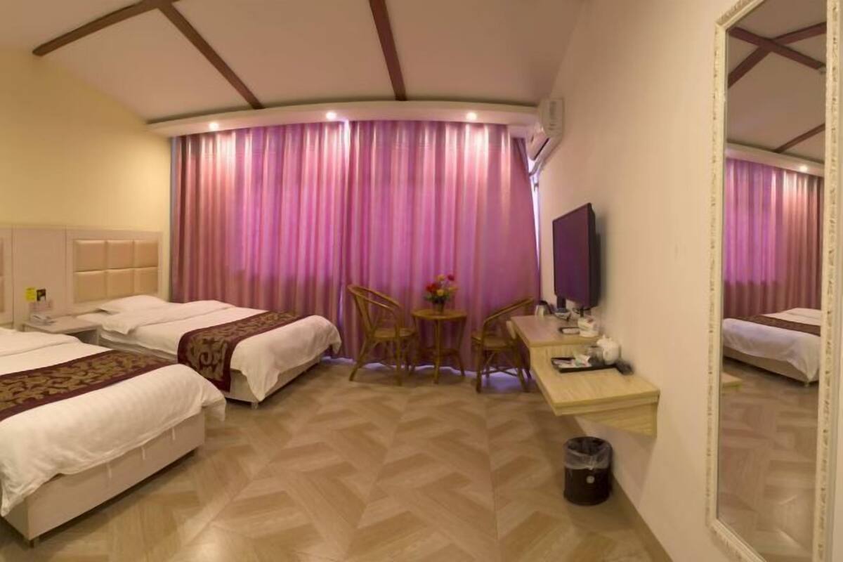 Una habitación de hotel con dos camas, un escritorio, una silla, un espejo y una cortina.